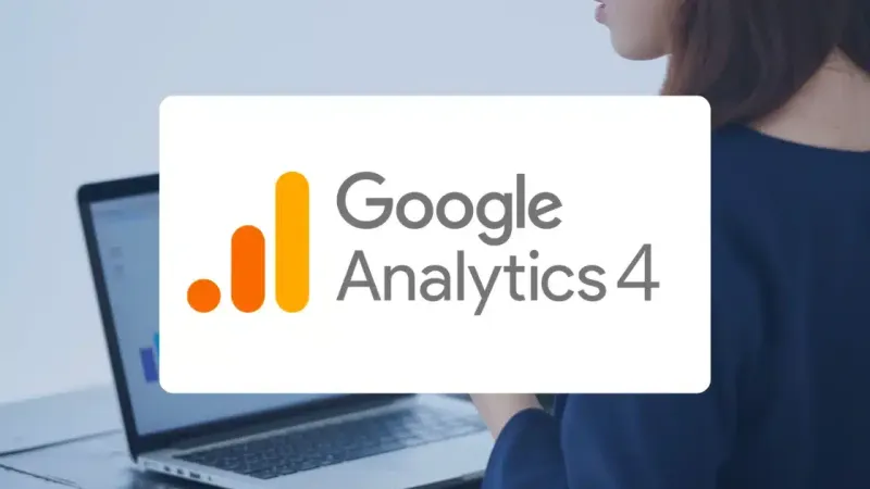 The Google Analytics 4 logo in front of a woman working on a laptop