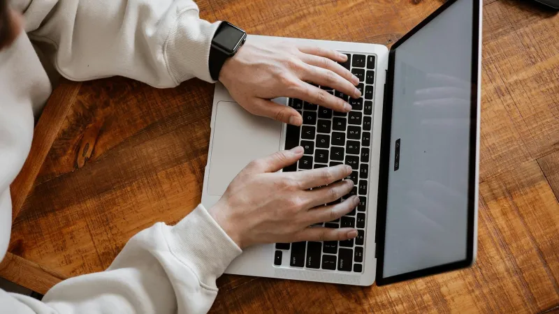Indonesian SEO content writer typing an article on a laptop at a wooden desk