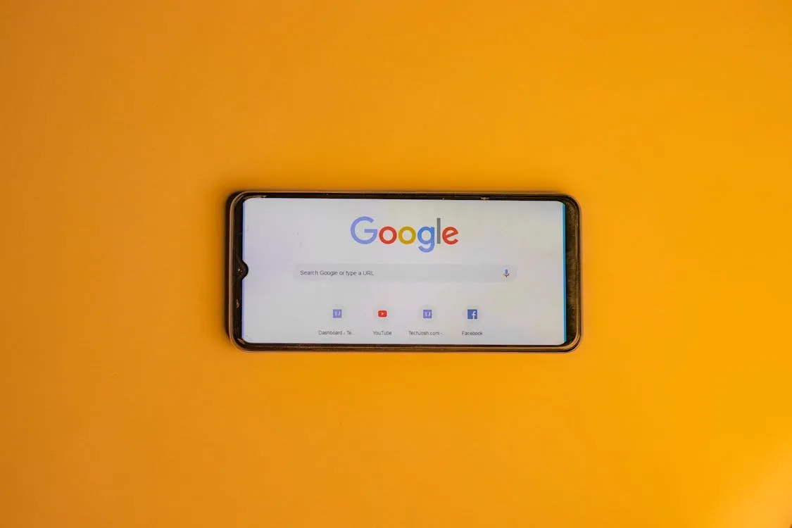 Smartphone showing the Google search page, lying on a yellow background