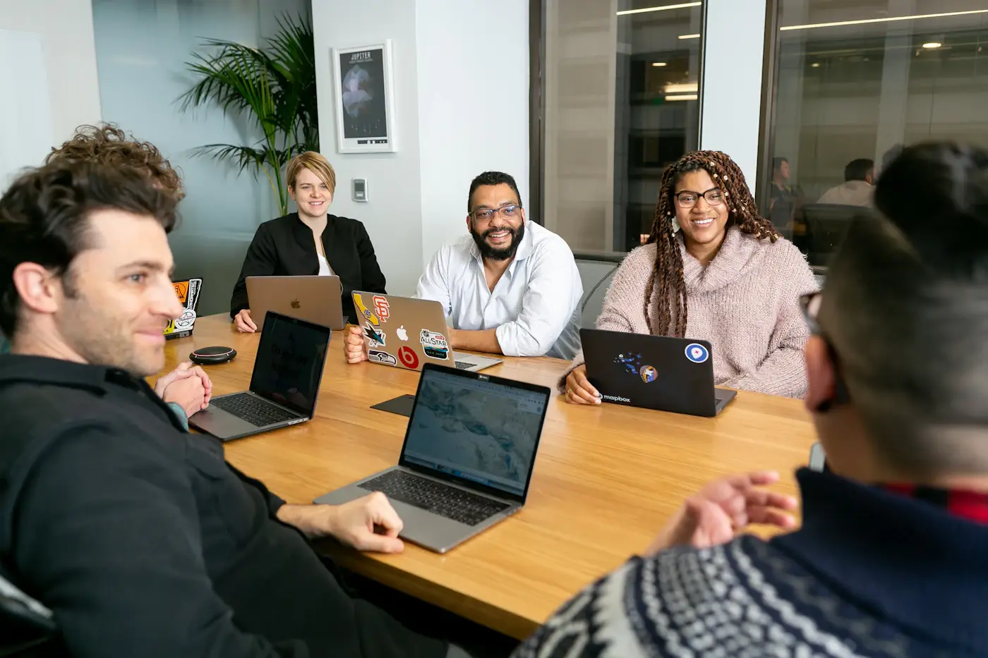 A team in discussion in a meeting room, each with a laptop