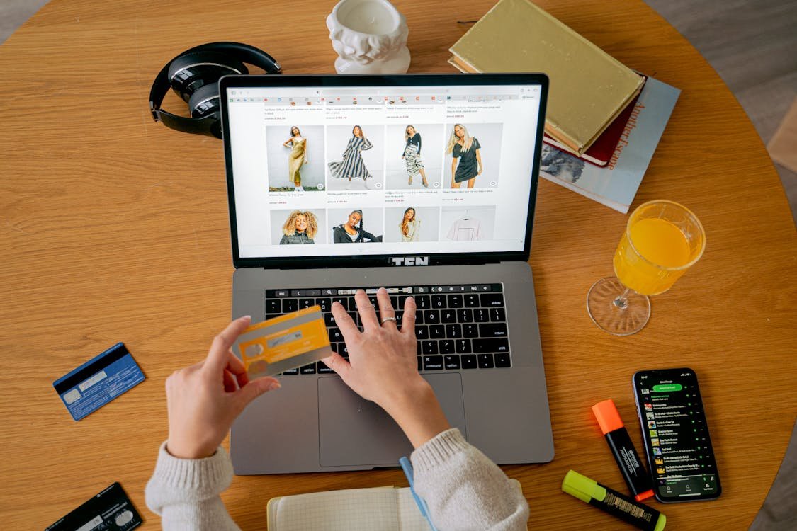 Wanita memegang kartu kredit sambil belanja di laptop